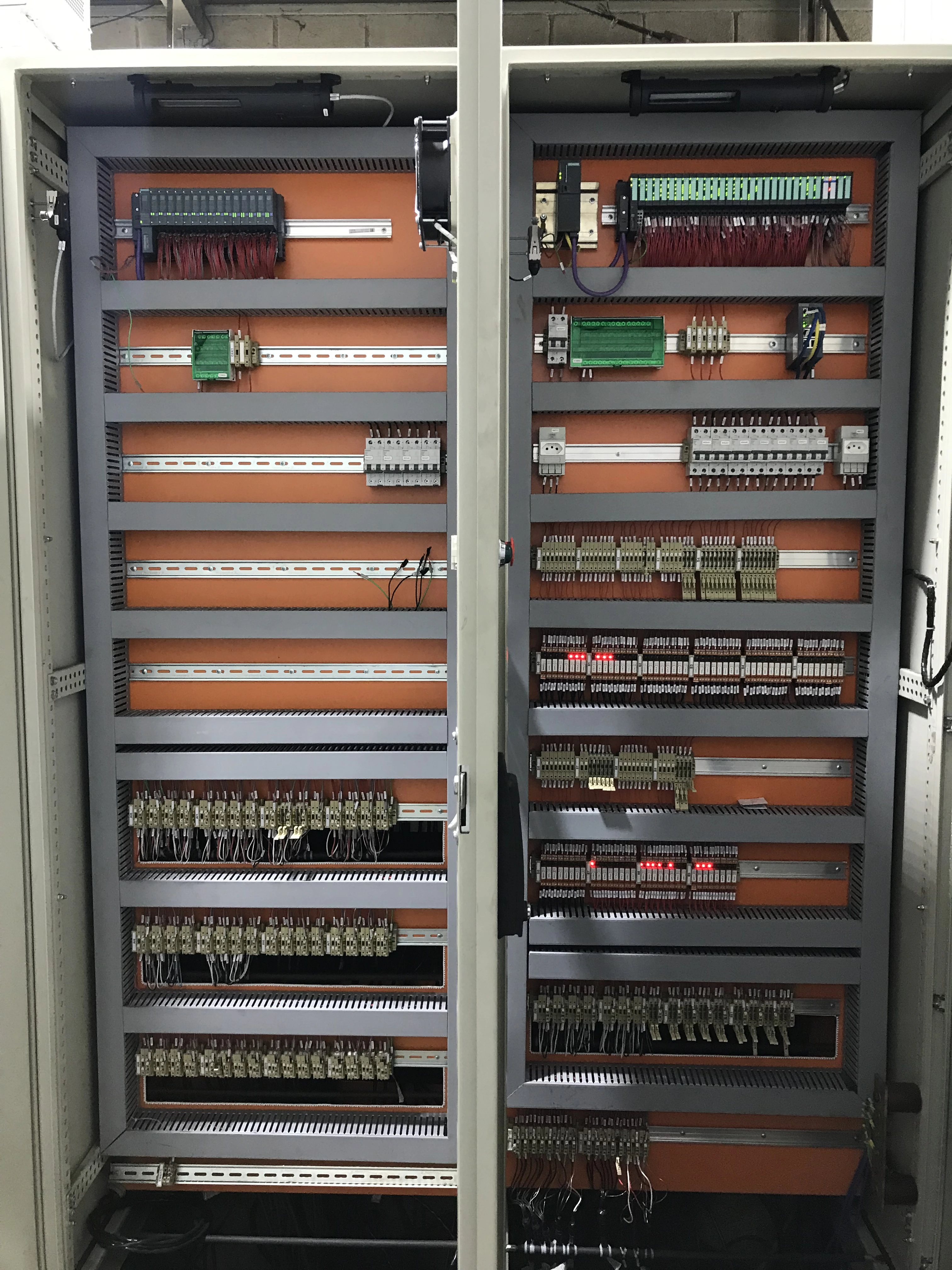 Fileira de painéis elétricos de comando montados lado a lado, destacando módulos PLC e bornes no topo do painel
